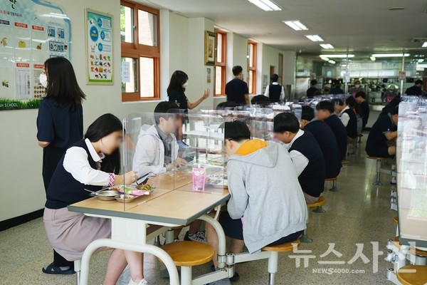 점심시간 투명 칸막이가 설치된 식탁에 지그재그로 앉아 식사 중인 학생들.